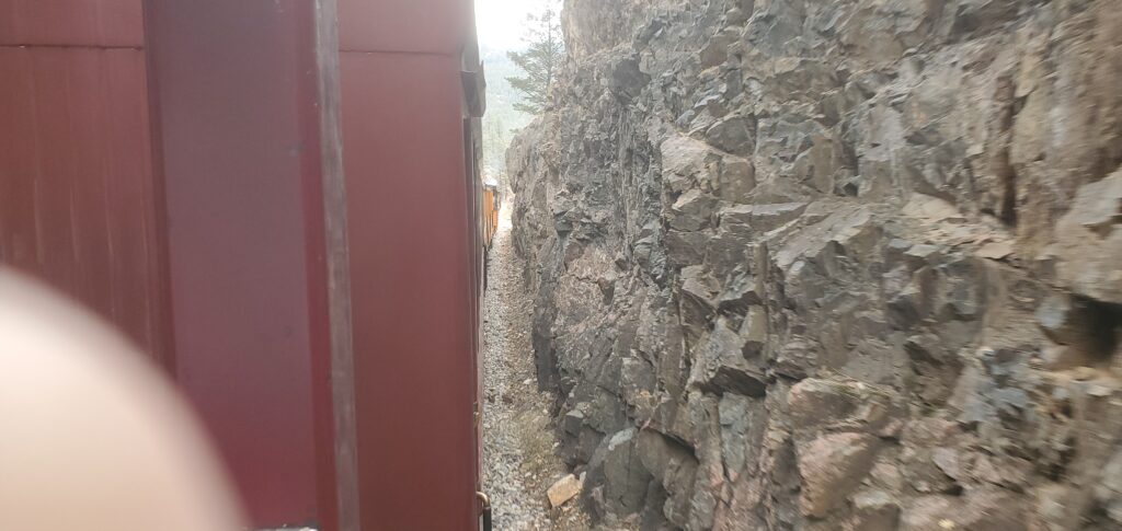 The train barely evades the rock face of a gouge in the mountain.