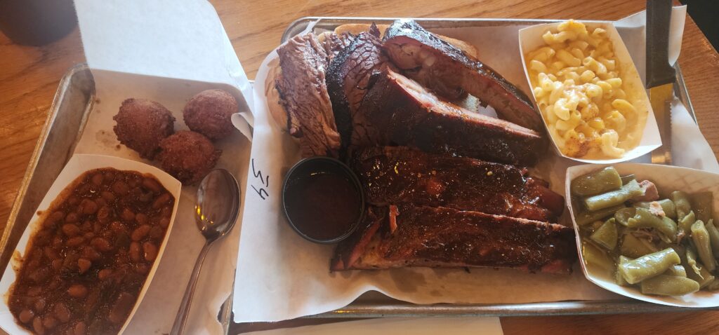 Plate of barbecue ribs, brisket, baked beans, hush puppies, macaroni and cheese and green beans